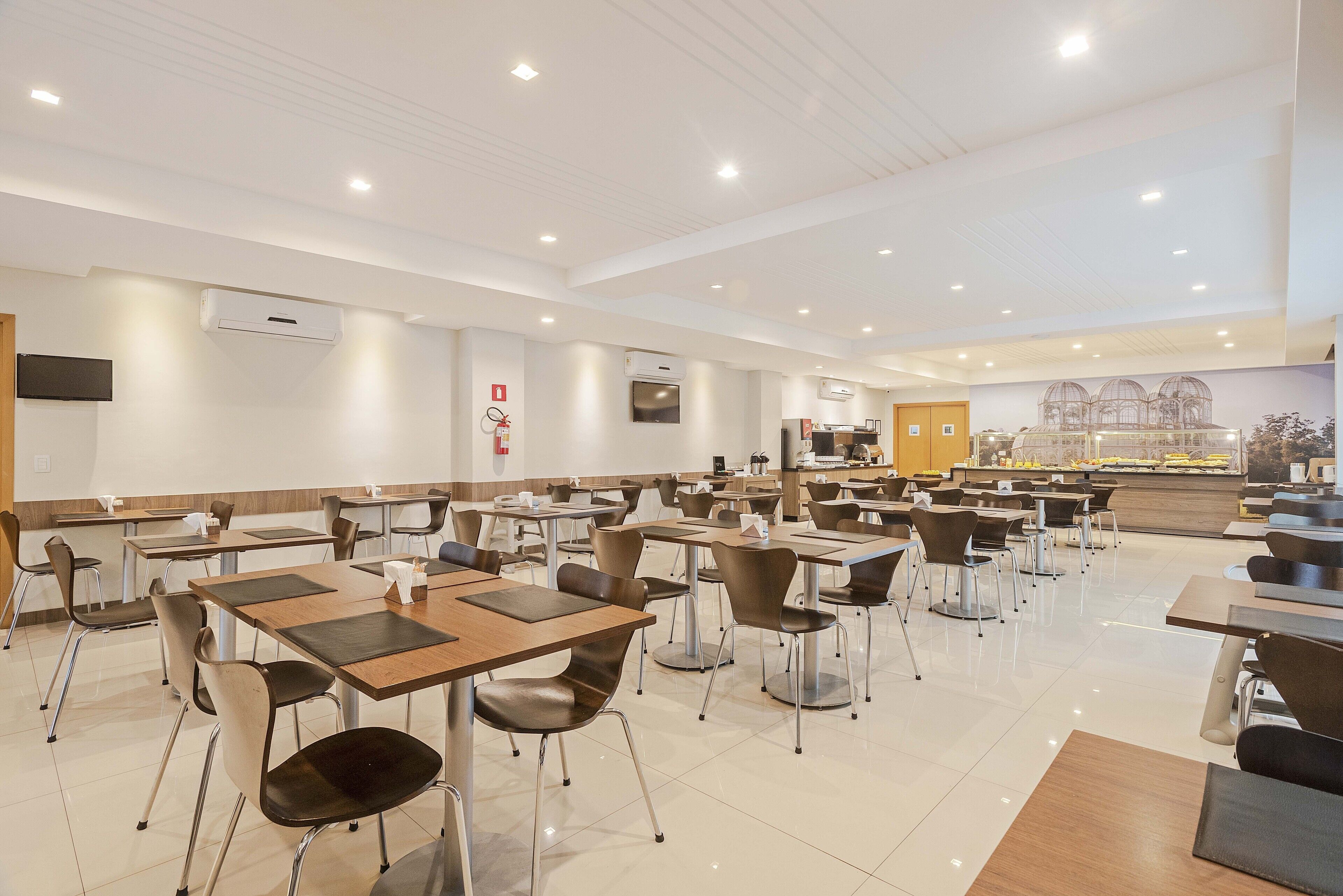 Un grand espace dédié à la salle à manger, avec de nombreuses tables et chaises, des climatiseurs fixés aux murs et un comptoir où sont présentés différents plats.