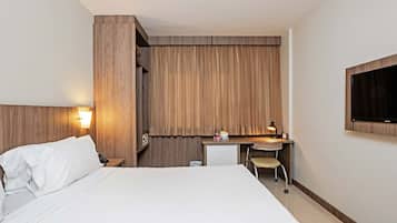 Une chambre d’hôtel équipée d’un lit, d’un bureau, d’une chaise, d’une télévision et d’un petit réfrigérateur.