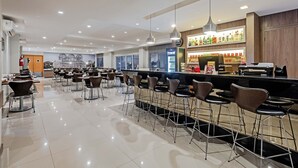 A modern bar area with high stools, a counter, and a variety of beverages on display.