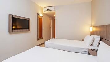 Habitació d'hotel amb dos llits individuals, televisió penjada a la paret, aire condicionat i una làmpada de nit.