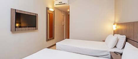 Habitación de hotel con dos camas individuales, un televisor montado, un equipo de aire acondicionado y una lámpara de noche.
