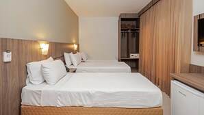 A hotel room with two beds, wooden paneling, a minibar, and a television.