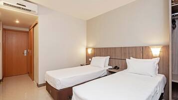 A hotel room with two single beds, a wooden headboard, a wall-mounted light, and a ceiling air conditioner.