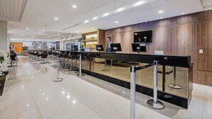 A modern hotel lobby with a reception desk, seating area, and a bar.
