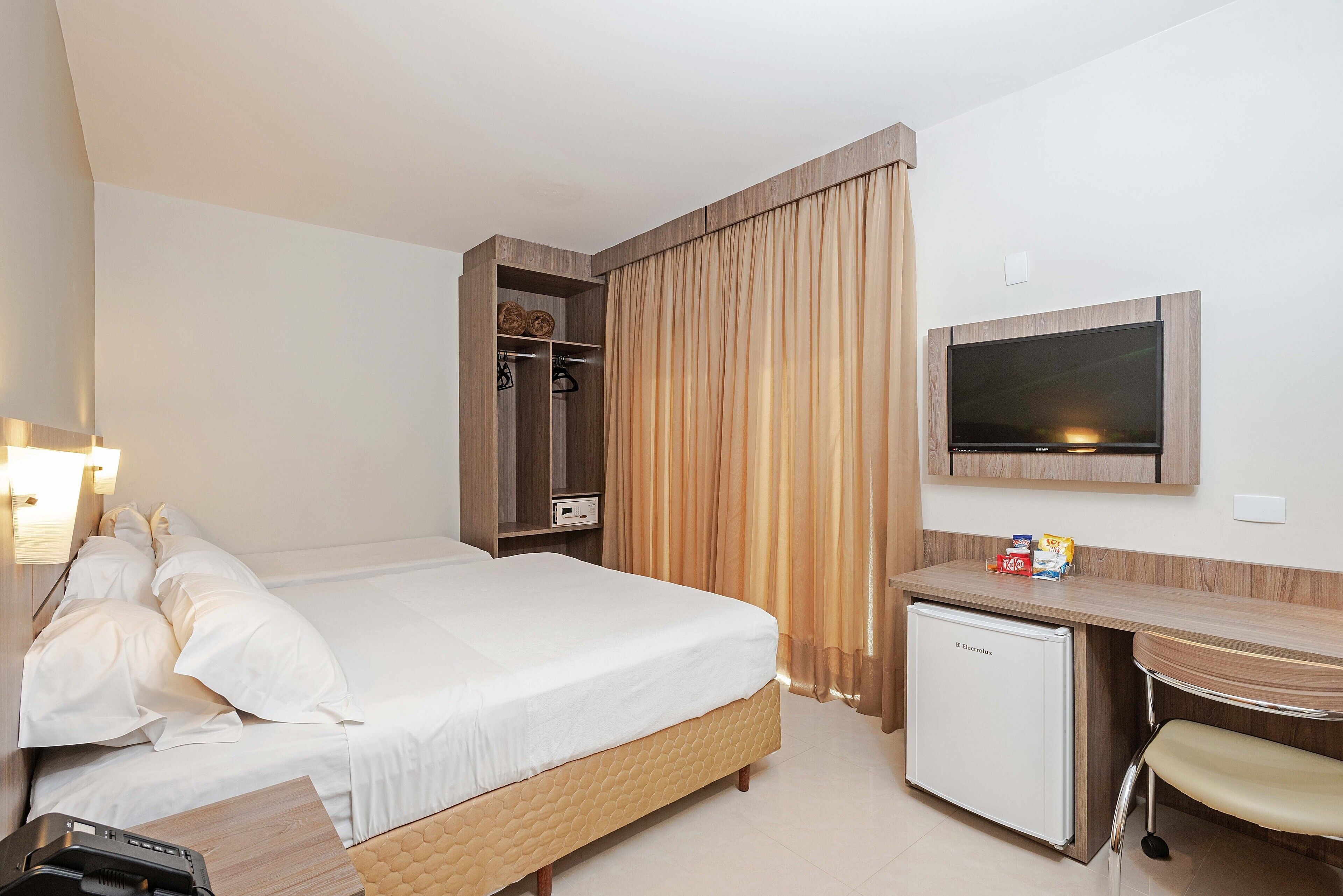A hotel room with a bed, a desk, a television, and a mini-fridge.
