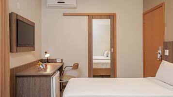 A hotel room with a bed, desk, chair, and a mirror.