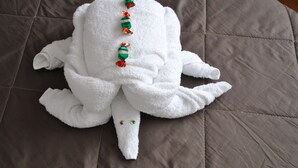 A white towel with a green and red striped pattern and a small plush toy resembling a bear on a brown quilted bed. - Stupor Mundi Bed and Breakfast (Palermo)