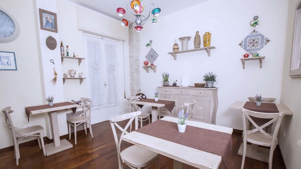 A dining area with wooden tables and chairs, a chandelier, decorative wall shelves, and a door. - Stupor Mundi Bed and Breakfast (Palermo)