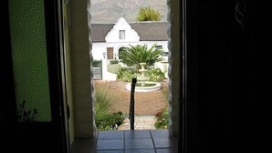 A doorway leading to a courtyard with a fountain, a white building, and mountains in the background. - Kingna Lodge (Montagu)