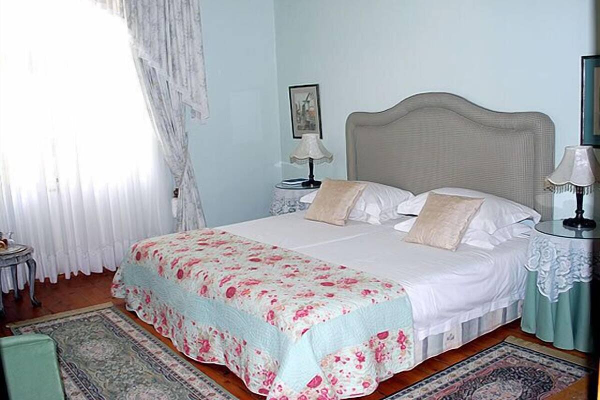 A bedroom with a bed, two bedside tables, a nightstand, a window with curtains, and a rug.