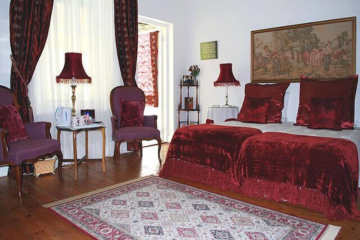 A room with a large bed, two chairs, a small table, and a painting on the wall.