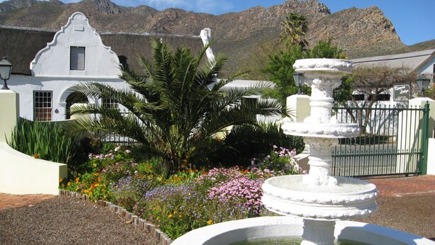 A white building with a fountain and a mountain in the background. - Kingna Lodge (Montagu)