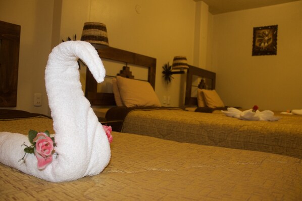 A hotel room with a bed featuring a swan-shaped towel and a pink rose decoration.
