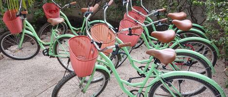 Una hilera de bicicletas verdes con cestas y sillines, estacionadas sobre un camino de grava.