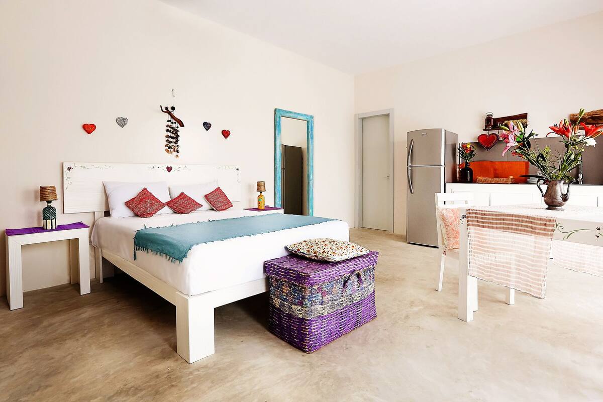 A bedroom with a bed, bedside tables, a dresser, and a kitchenette.