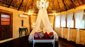A bed with a canopy, a wooden door, a small table, and a window with curtains. - Xscape Tulum (Tulum)