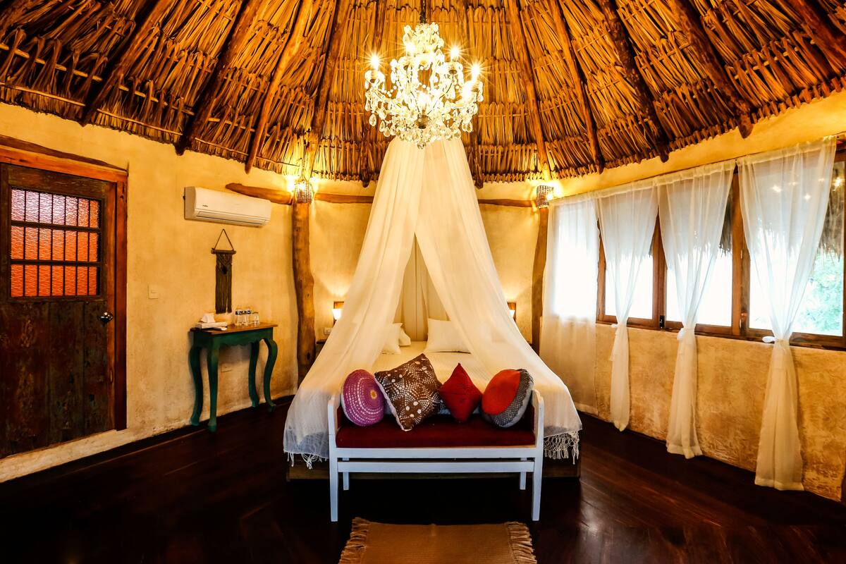 A bed with a canopy, a wooden door, a small table, and a window with curtains.