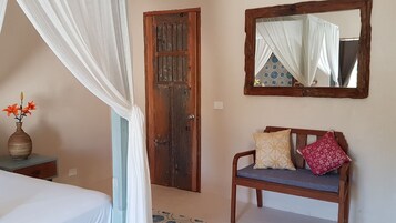 Een slaapkamer met een bed, een nachtkastje met een vaas, een houten deur, een bank met kussens en een spiegel aan de muur.