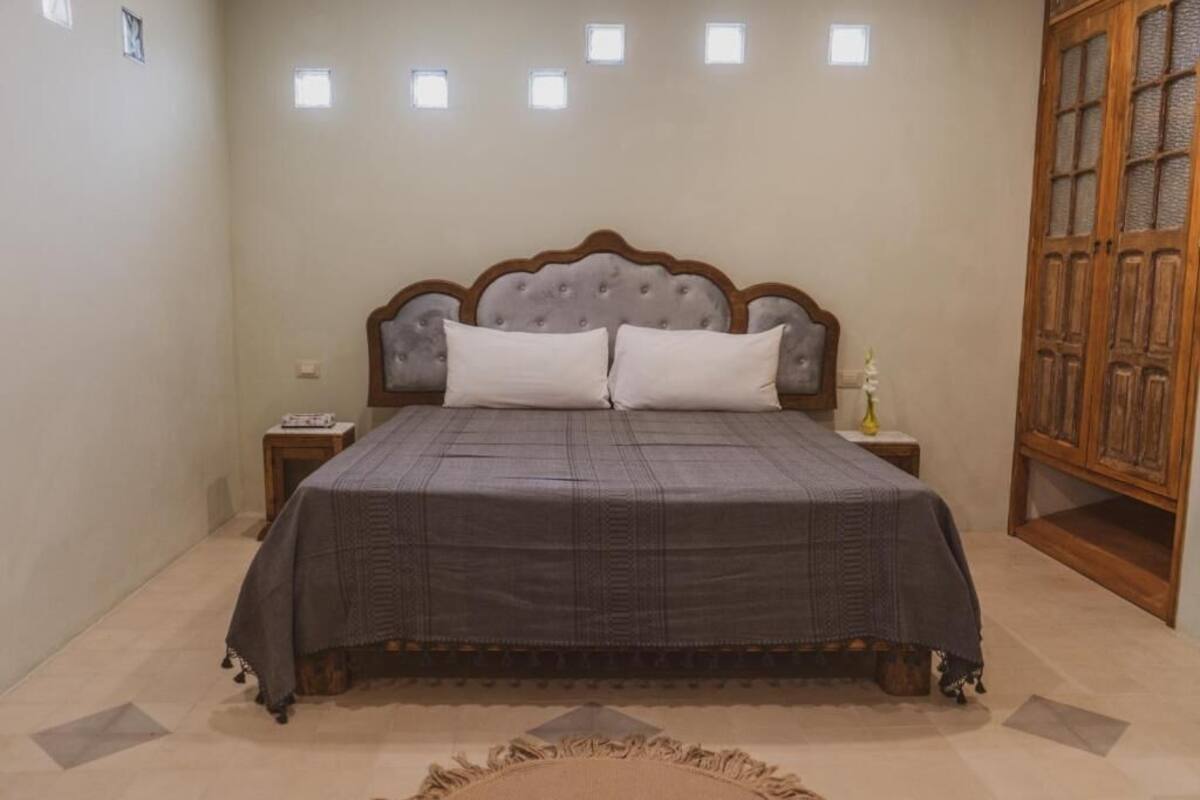 A bedroom with a large bed, a nightstand, a wooden wardrobe, and a small table with a vase.