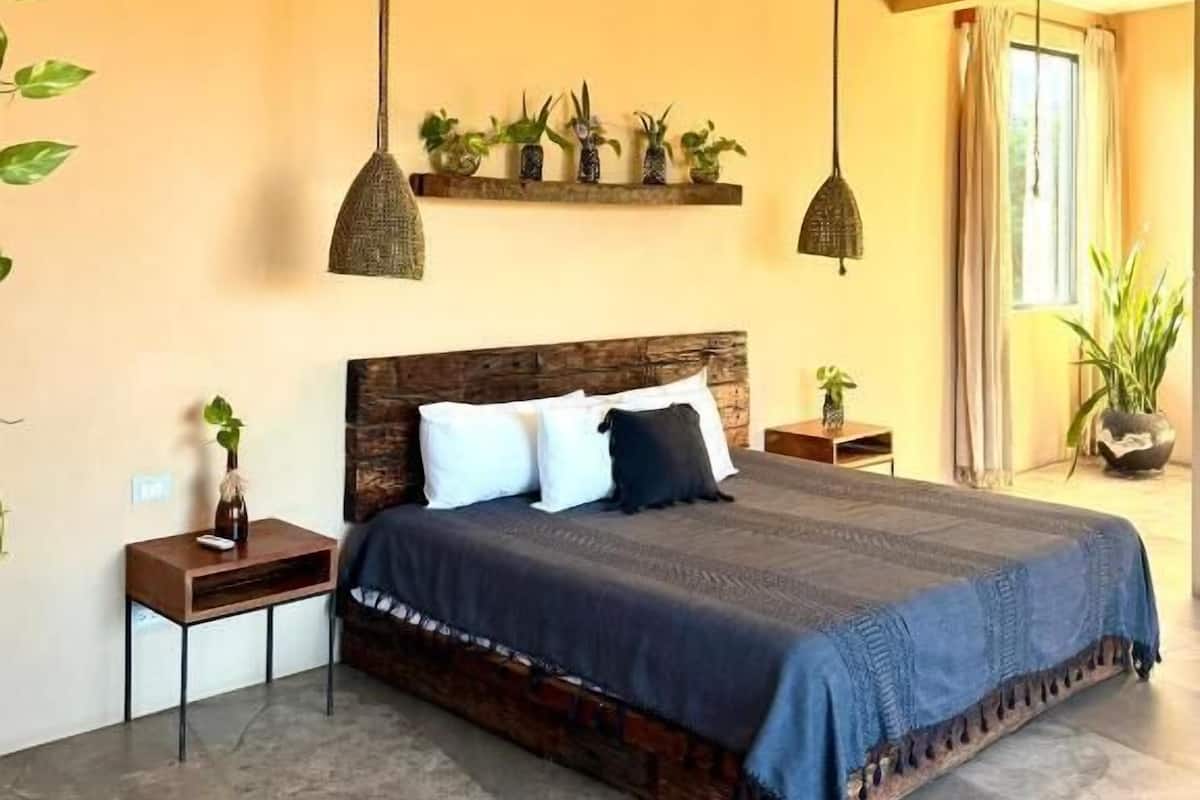 A bedroom with a large bed, a wooden headboard, a bedside table with a lamp, and a window with curtains.