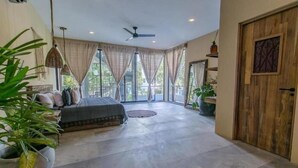 A spacious room with a large bed, a ceiling fan, and a view through large windows. - Xscape Tulum (Tulum)