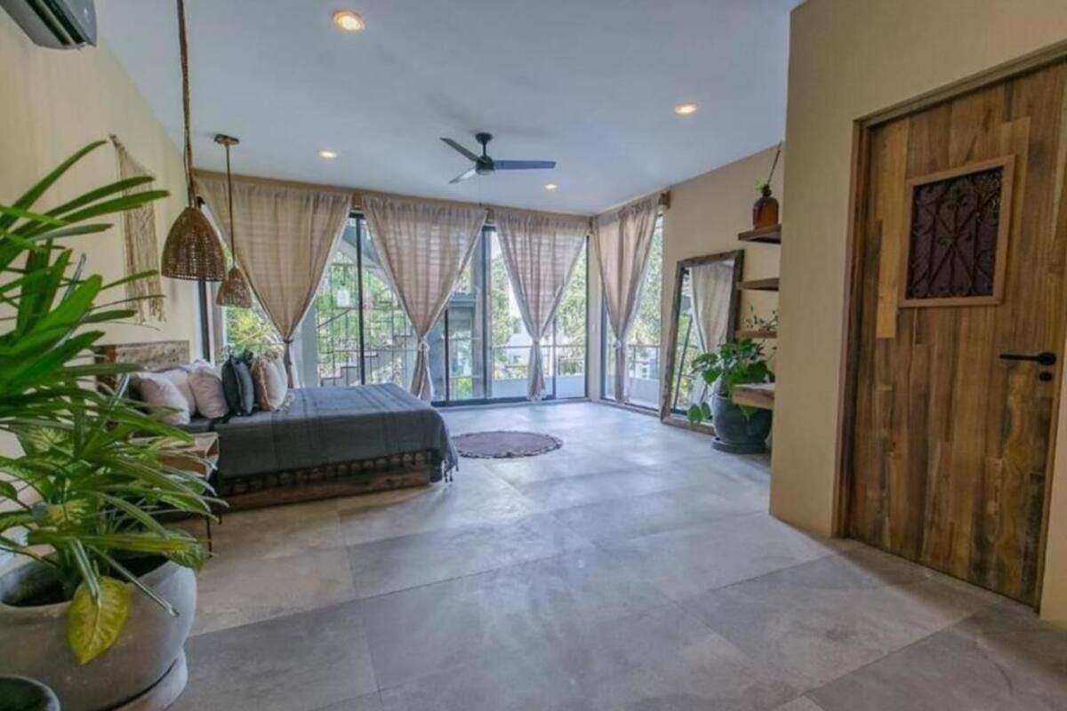 A spacious room with a large bed, a ceiling fan, and a view through large windows.