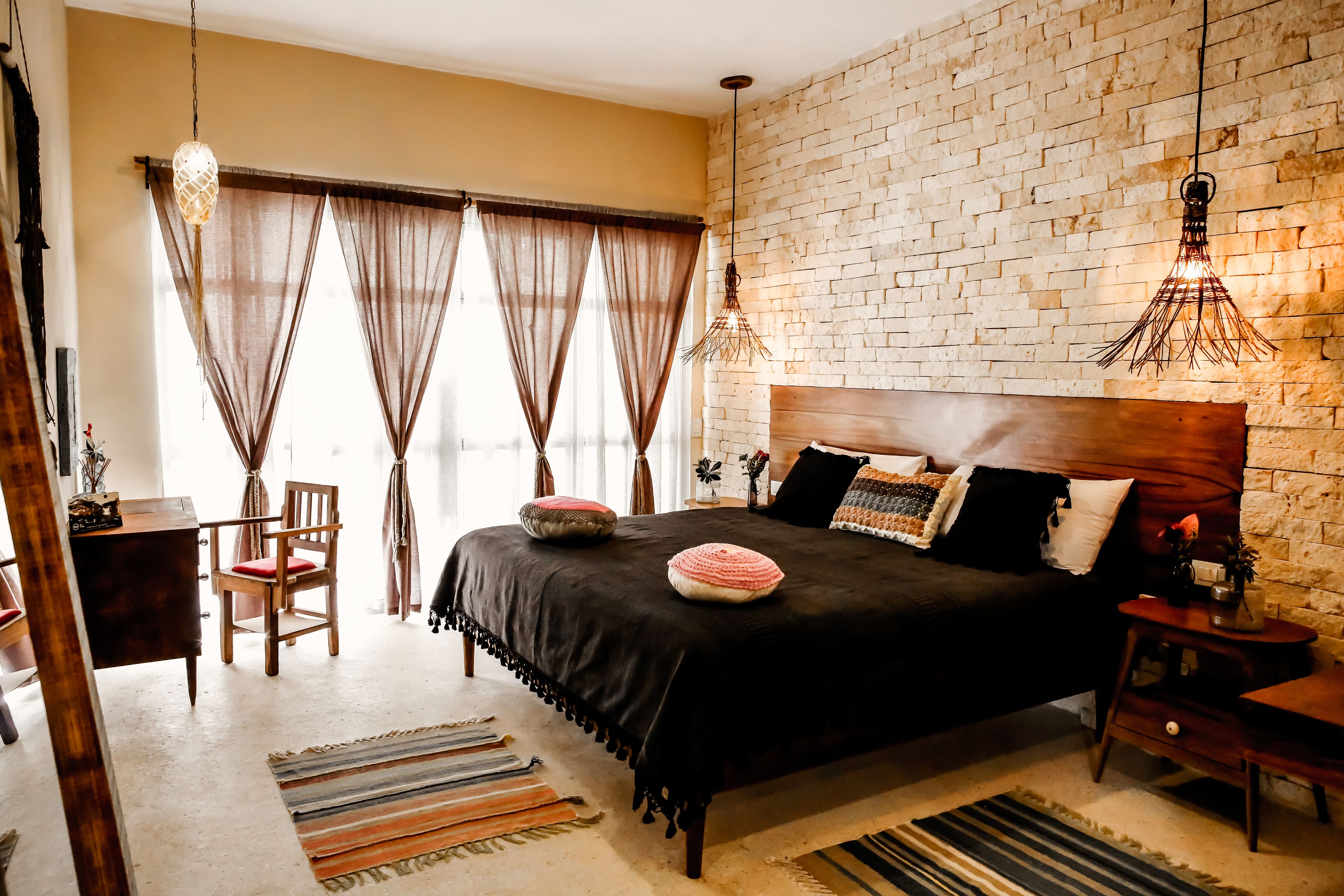 Un dormitorio con pared de ladrillo, una cama grande con muchas almohadas, una mesita de noche de madera y un escritorio con una silla.