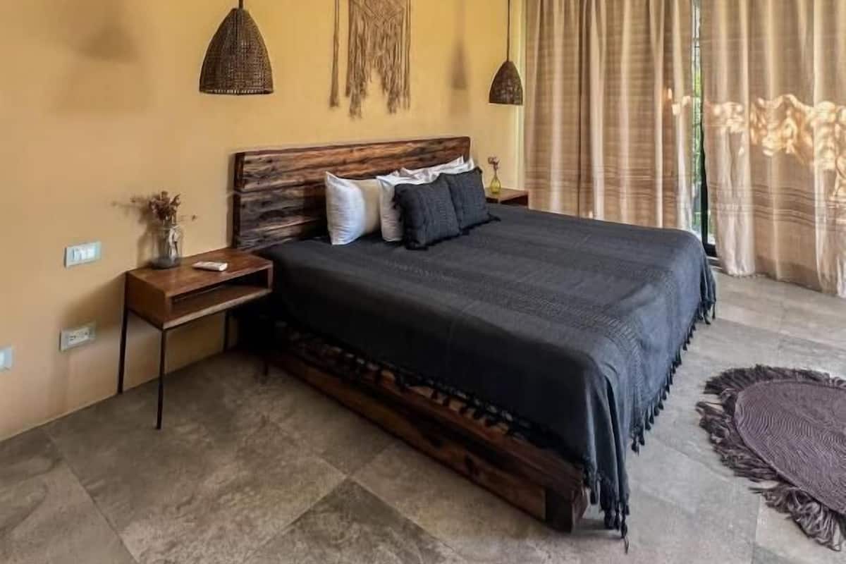 A bedroom with a large bed, two bedside tables, a ceiling fan, and a window with curtains.