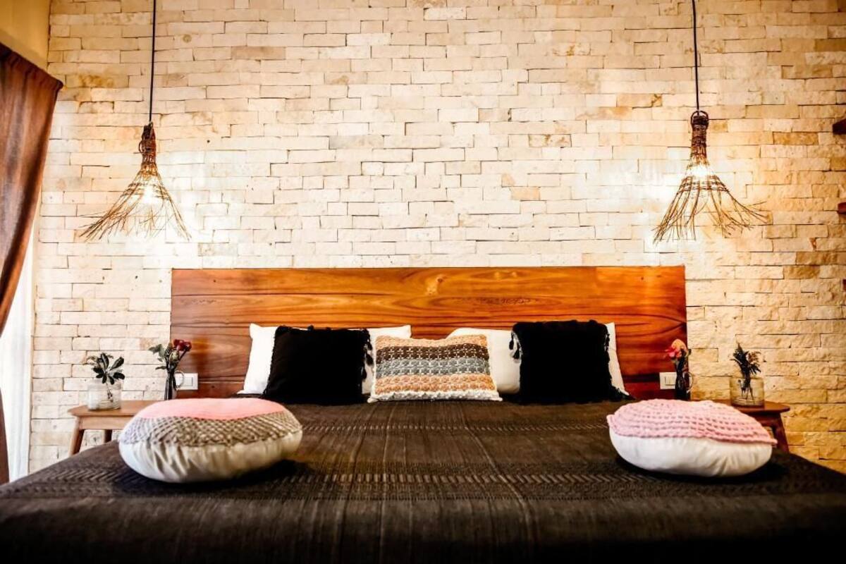 A bedroom with a brick wall, a wooden headboard, and two hanging light fixtures.