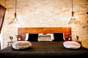 Une chambre avec un mur en briques, une tête de lit en bois et deux luminaires suspendus.