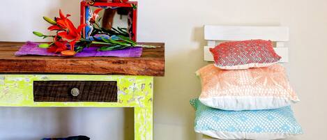 A room with a wooden shelf holding a decorative item and a small white chair with multiple cushions.