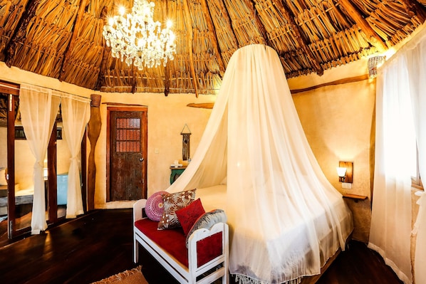 A room with a thatched roof, a bed with a white canopy, and a chandelier.
