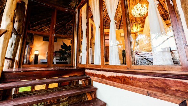 A wooden staircase leading to a room with large windows, a chandelier, and a rustic ceiling. - Xscape Tulum (Tulum)