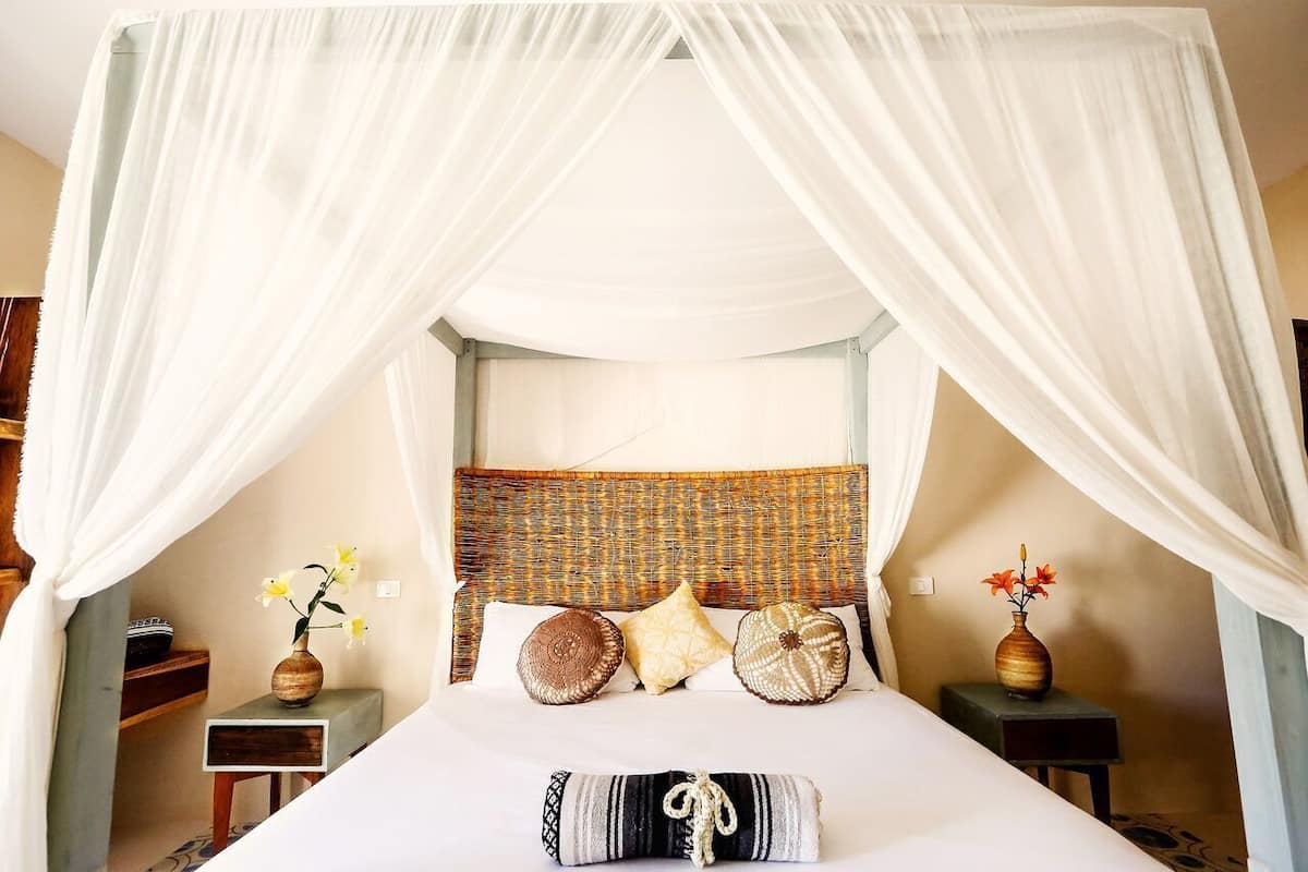 A bed with a canopy, a woven headboard, and two bedside tables with vases.
