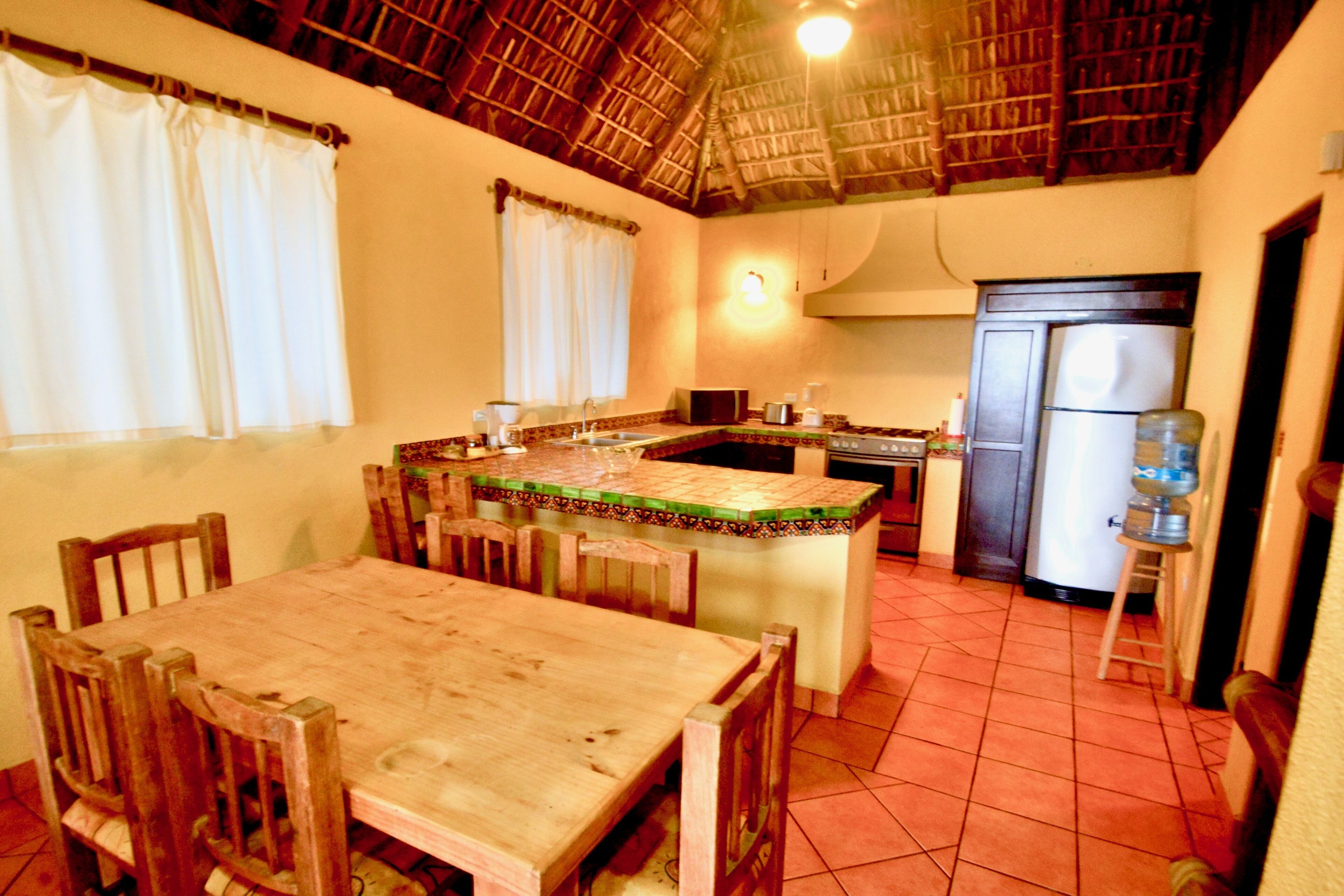 A kitchen with a wooden table and chairs, a water dispenser, and a refrigerator.