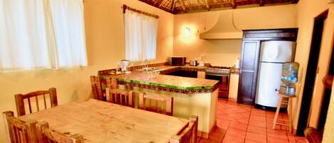 A kitchen with a wooden table and chairs, a water dispenser, and a refrigerator.