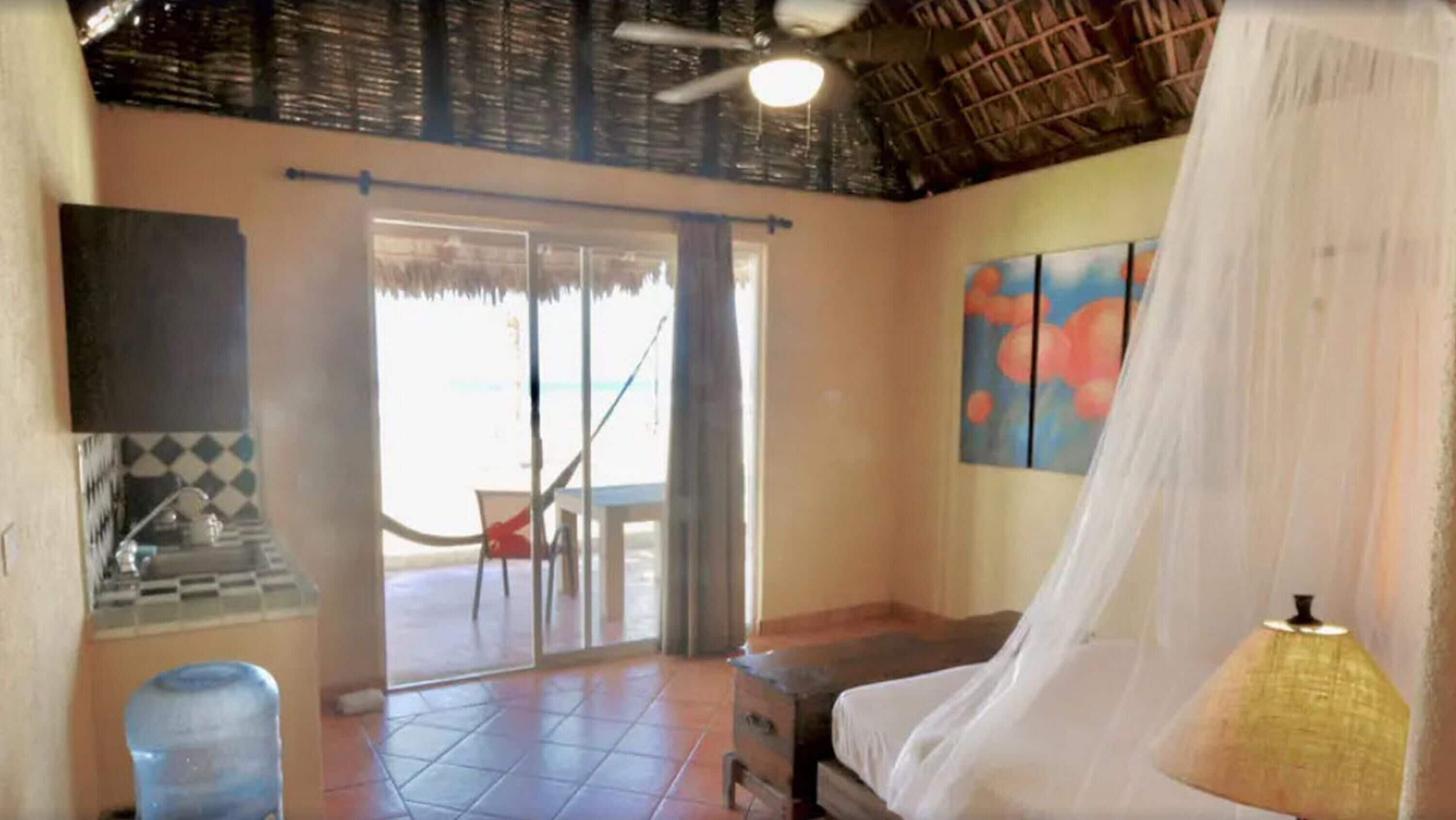 A room with a bed, a TV, a water dispenser, and a view of the beach through a glass door.