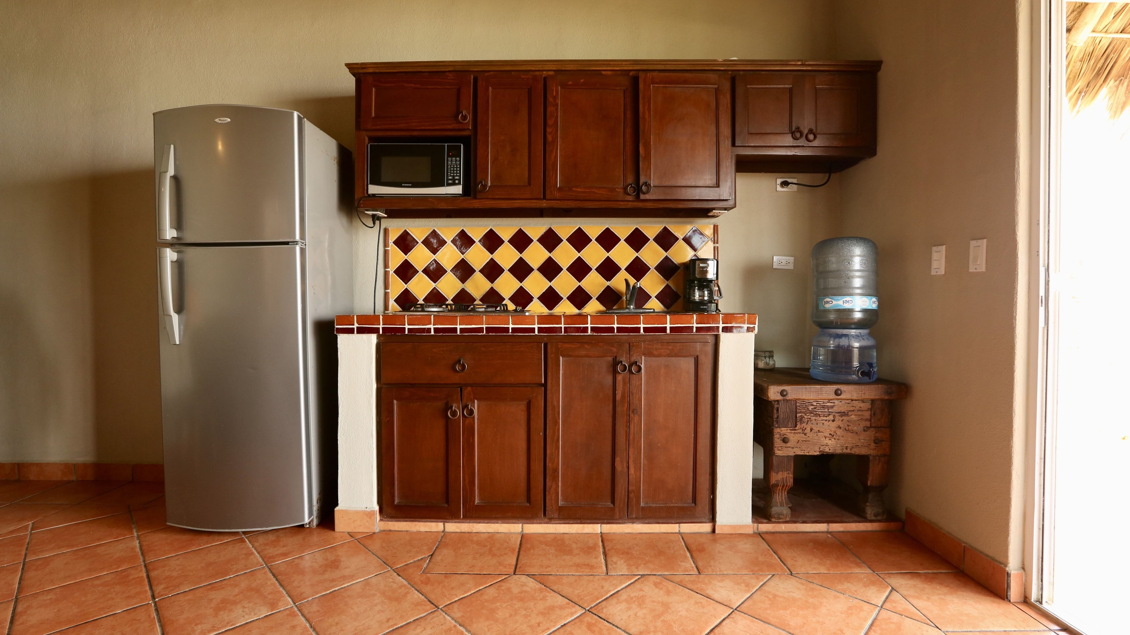 A compact kitchen with a refrigerator, microwave, wooden cabinets, and a tiled backsplash.