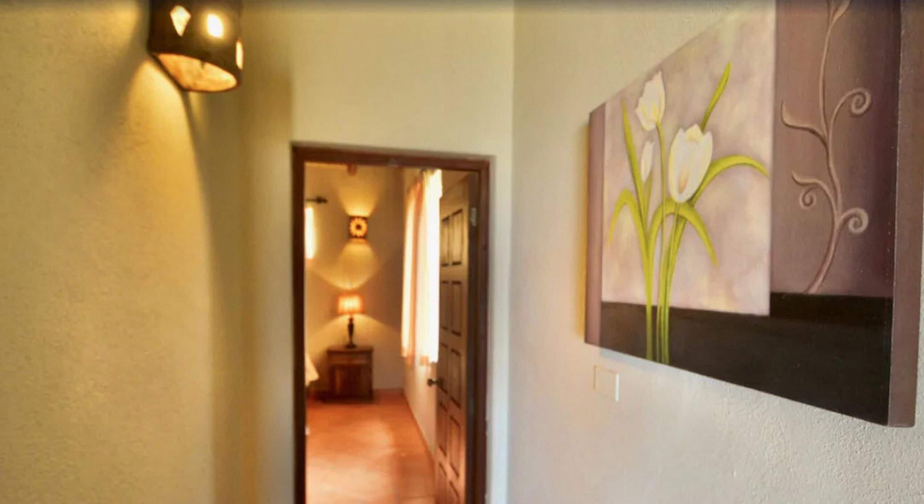 A hallway with a lamp, a painting of flowers, and a door.