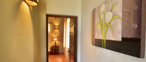 A hallway with a lamp, a painting of flowers, and a door.