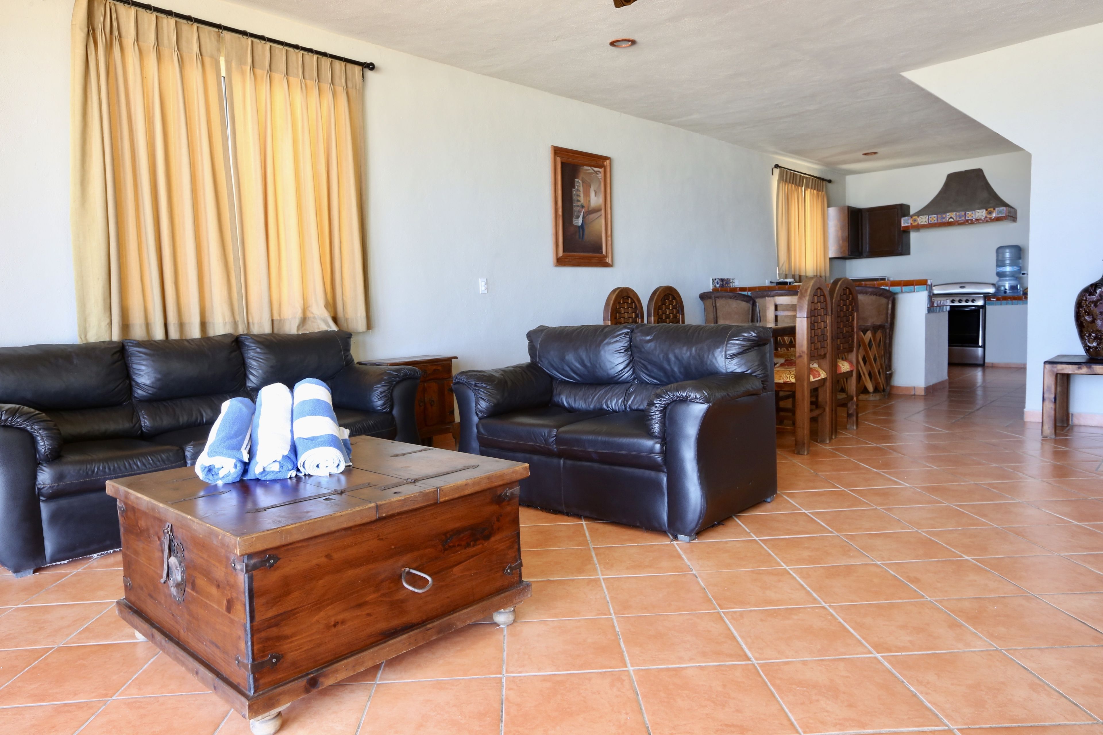 Una sala de estar con dos sofás de cuero negro, una mesa de centro de madera y un comedor con mesa y sillas de madera.