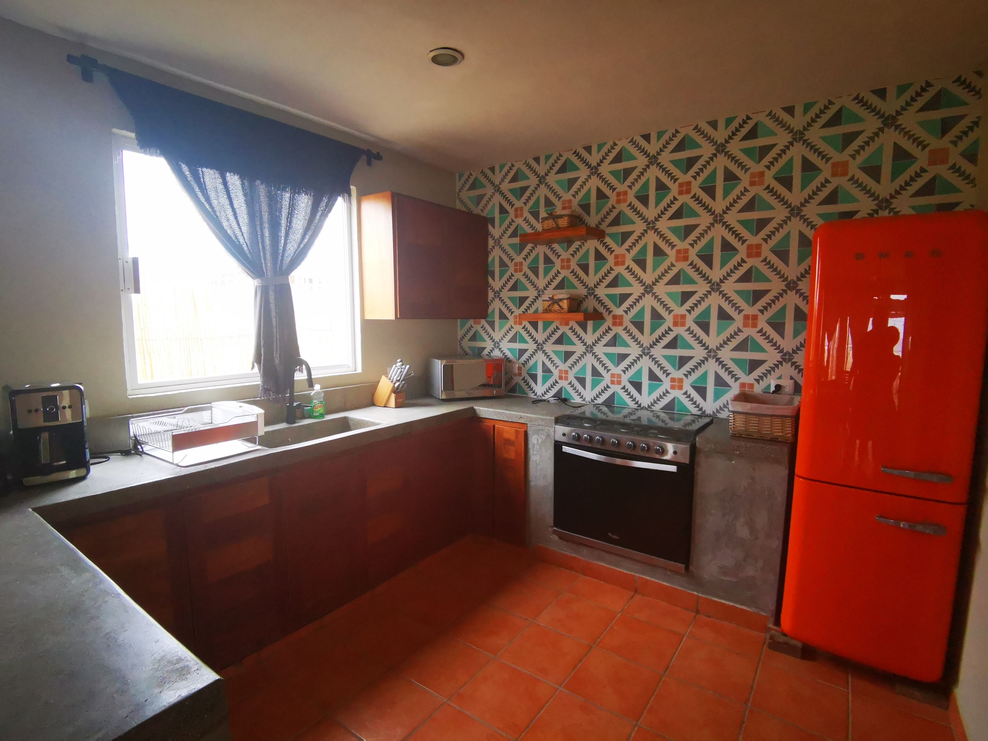 A compact kitchen with a sink, stove, and a red refrigerator.