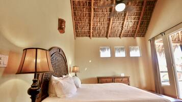 A bedroom with a bed, two bedside lamps, a wooden headboard, a ceiling fan, and a window with curtains.
