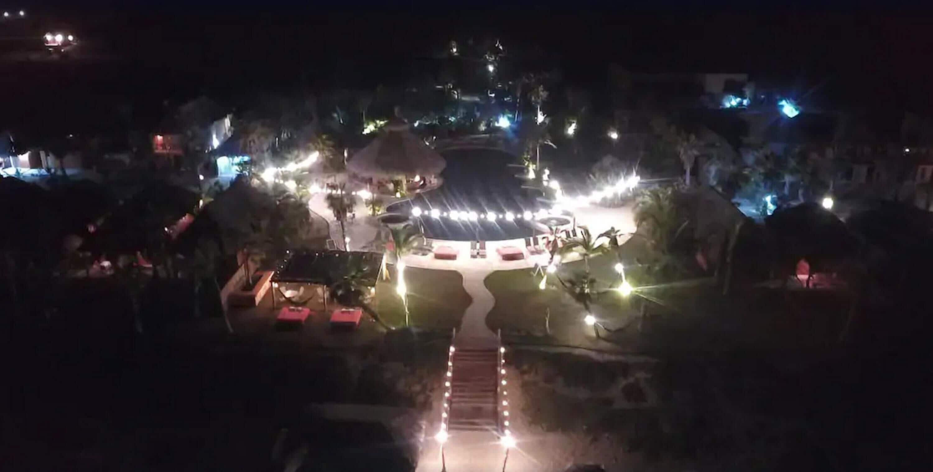 A nighttime view of a resort with a central pavilion, pathways, and surrounding vegetation.