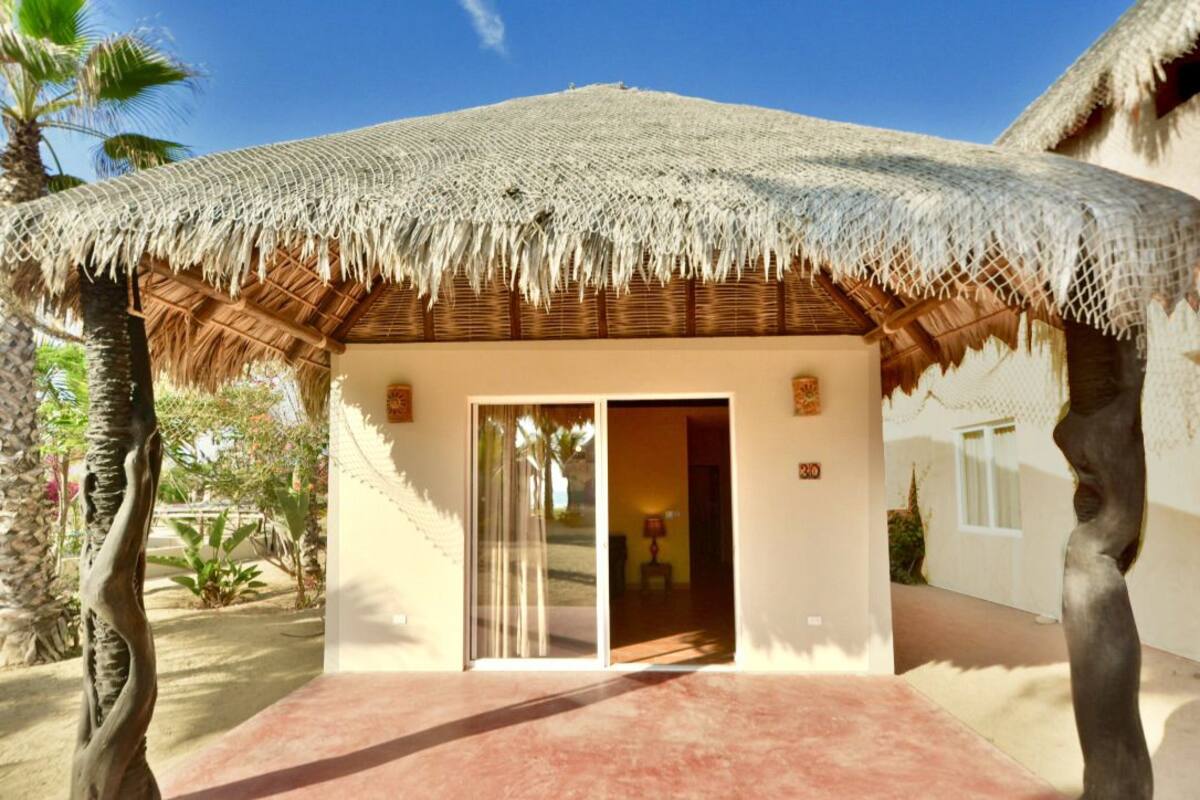 Un bungalow doté d’un toit de chaume, d’une porte-fenêtre coulissante et d’un petit espace patio.