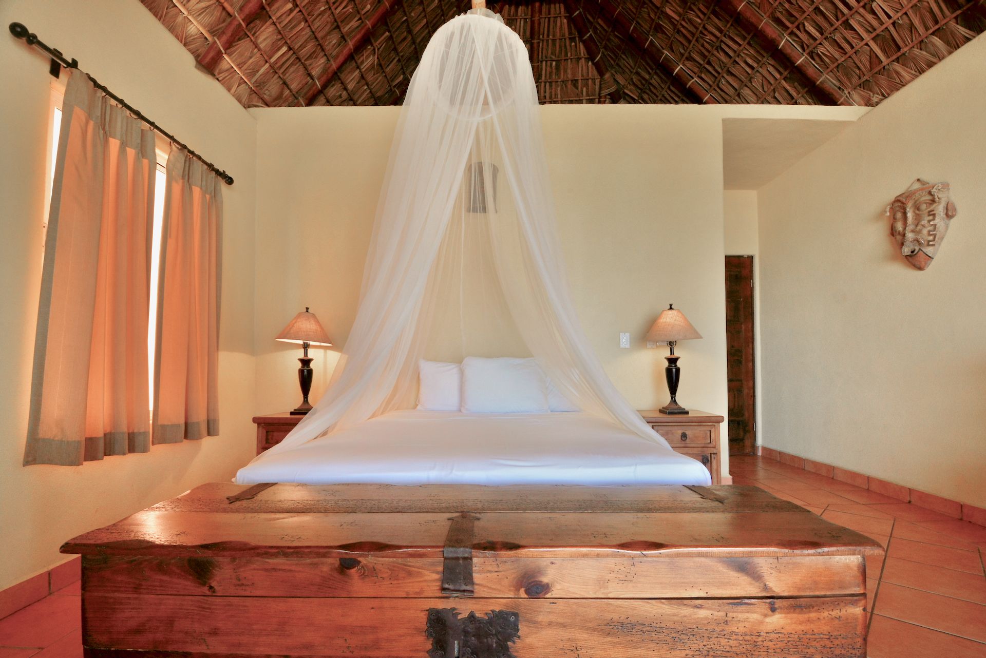 A bed with a canopy, wooden headboard, two bedside tables with lamps, and a rustic wall decor.