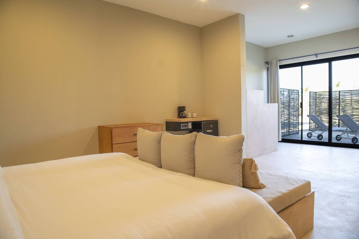 Une chambre d’hôtel avec un grand lit, une commode en bois, un petit bureau avec une machine à café et une vue sur le balcon extérieur.