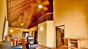 A spacious living area with a high ceiling, a leather sofa, a wooden coffee table, and a bookshelf. - Cerritos Surf Town Beach Front Hotel and SPA (El Pescadero)