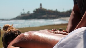A person receiving a back massage on a beach with a view of a distant island. - Cerritos Surf Town Beach Front Hotel and SPA (El Pescadero)