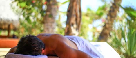 A person receiving a massage in a room with a view of palm trees and greenery.